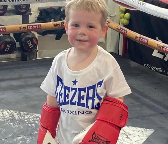 Little boy smiling with red boxing gloves on in a boxing ring